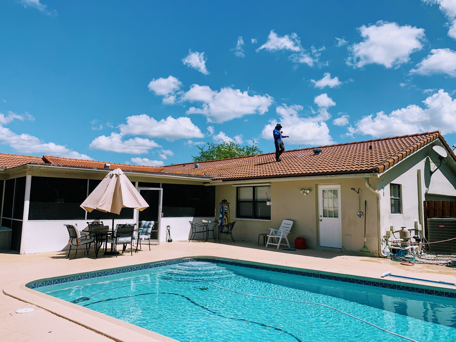 Crew member soft-washing a tile roof above the pool